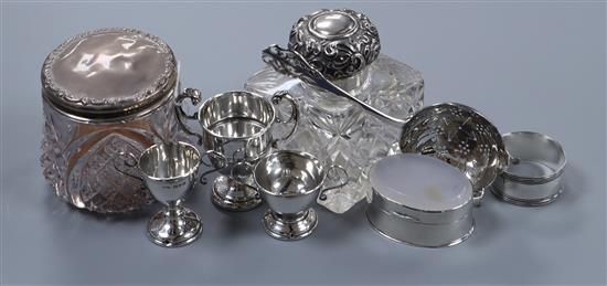 A silver tea strainer, three miniature silver trophy cups, a silver pill box, napkin ring, scent bottle and mounted toilet bottle.